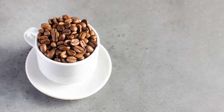 Roasted coffee beans in a white mug on a grey background.
