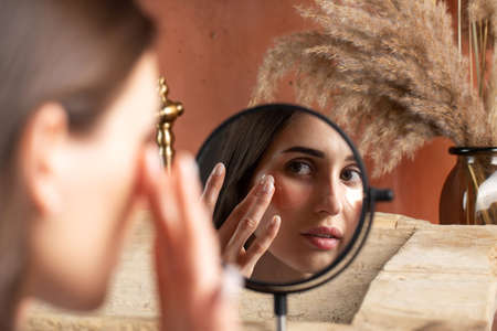 Mirror reflection of woman applying under-eye patch at dressing table closeupの写真素材