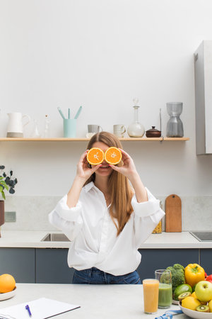 An attractive girl smiles and closes her eyes with orange halves in the kitchen. The concept of diet, vegetarianism.の写真素材