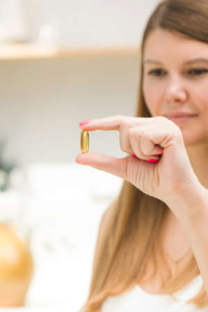 A woman holds in her hand a yellow transparent capsule with vitamin D or omega-3 in close-up....