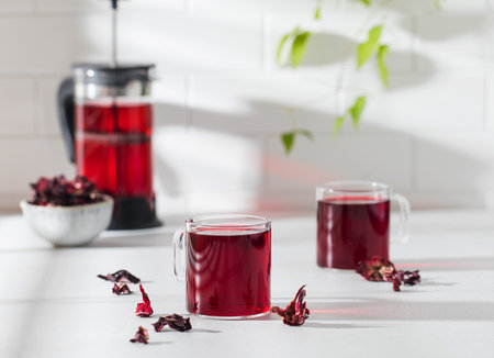 Herbal tea made from hibiscus petals in a transparent cup on a light background and a bowl of dry hibiscus.の写真素材