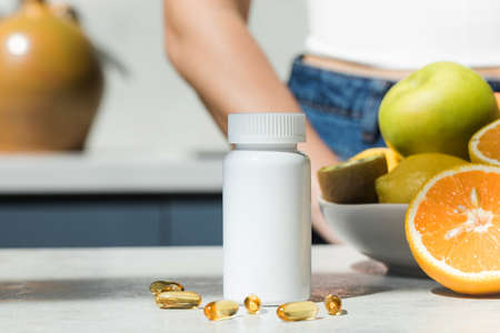 Mockup of a white plastic jar with vitamin D or fish oil capsules on the kitchen table. Nutritional supplements.の写真素材