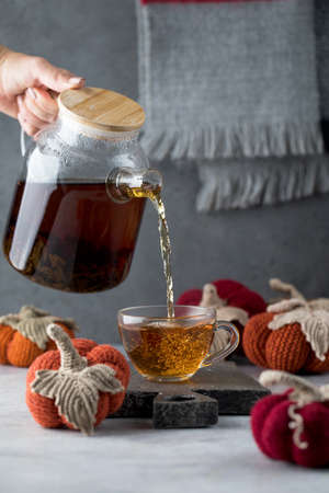 Black tea is poured into a mug from a teapot with knitted decorative pumpkins. Autumn and coziness....