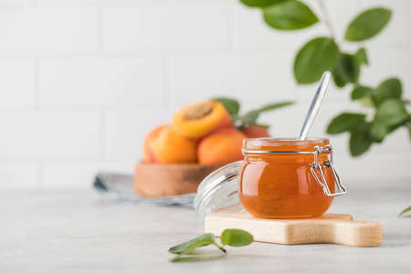 A jar of apricot jam with a spoon inside, ripe apricots in a plate and a branch with green leaves. Fruit preservation.の写真素材