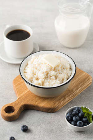 Rice porridge or pudding with a piece of butter, a mug of coffee and blueberries in a bowl. Healthy breakfast.の写真素材