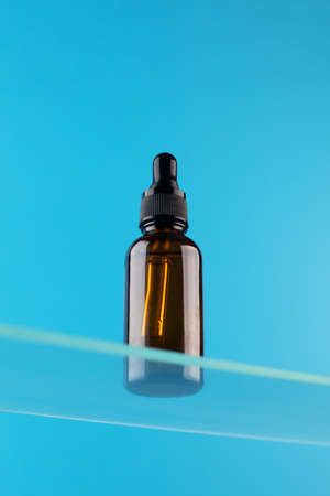 Brown glass dropper with anti-aging care cosmetics on a glass shelf.の写真素材