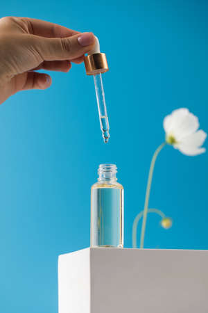 A woman with a pipette drips skin care serum into a transparent dropper, which stands on a podium on...