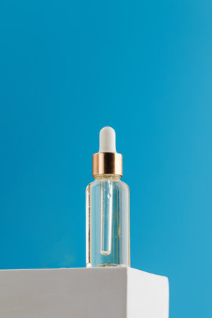A transparent glass dropper with a cosmetic product on a podium on a blue background.の写真素材