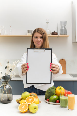 Woman is holding a blank tablet for your text, standing at the table with fresh fruits and vegetables.の写真素材