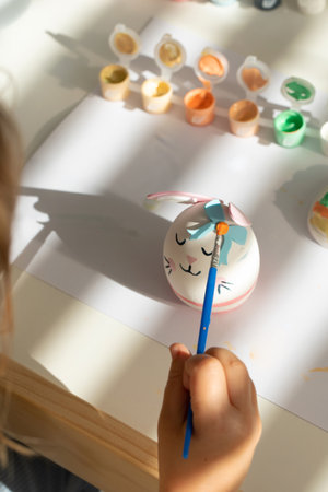 A cute little girl is decorating an Easter egg in the form of a rabbit. Creativity and hobbies.の写真素材