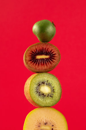 Still life with balancing kiwis of different varieties on a red. A balance of fruits, a modern and art concept.の写真素材