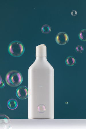 A white mock-up of a bottle with cosmetics on a white shelf with flying soap bubbles.の写真素材