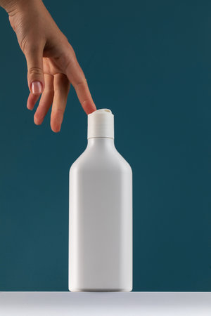 A womans hand reaches for a bottle of cosmetics. White mock-up with shower gel with a place for your...