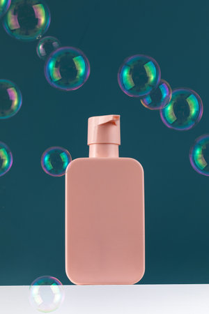 Empty pink plastic dispenser bottles with soap or shampoo on a white shelf with flying soap bubbles.の写真素材