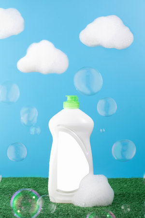 White bottle with dishwashing gel and place for your on a blue background with clouds of foam and soap bubbles.の写真素材
