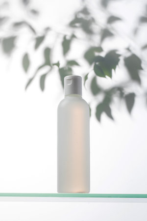 A bottle with a natural cosmetic product on a glass shelf and a shadow on the plants.の写真素材