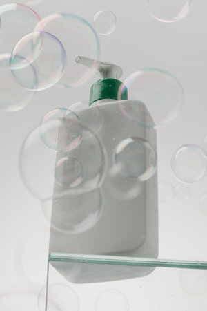 A white bottle with cosmetics on a glass shelf surrounded by flying bubbles. Shower gel, shampoo.の写真素材