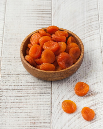 Dried apricots in a wooden bowl on a white wooden background. Dried fruits.
