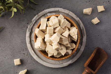 Pieces of organic white chocolate in a wooden bowl on a dark grey background. Oganic chocolate.の写真素材