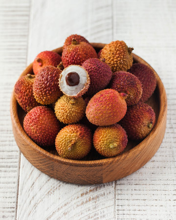 Lychees whole and half in a wooden bowl on a wooden background. Exotic fruits.の写真素材