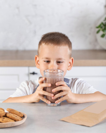 A cute boy is drinking cocoa from a glass cup in the kitchen. Chocolate milkの写真素材
