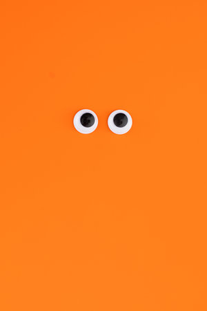 Funny plastic eyes on an orange background. Halloween greeting card
