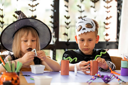 Cute brother and sister in Halloween costumes make festive crafts at the table. A master class on Halloween crafts.の写真素材