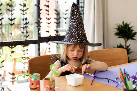 A cute girl in a witch costume makes a funny spider for Halloween with her own hands. Childrens...