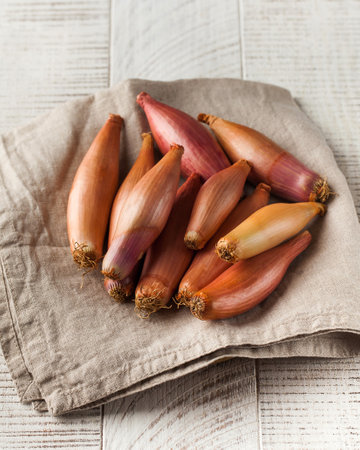 A pile of shallots on a napkin on a white wooden background. Vegetablesの写真素材