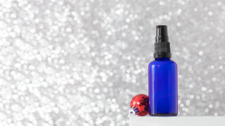 Dispenser with serum or oil for youthful skin on a silver background with a Christmas ball. Skin careの写真素材