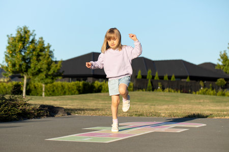 A cute girl is playing hopscotch on the asphalt in the playground. Active leisure for children.の写真素材