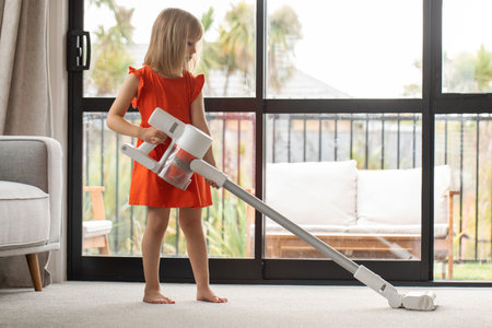A girl vacuums the living room with a modern wireless vacuum cleaner. Cleaning, wireless technologyの写真素材