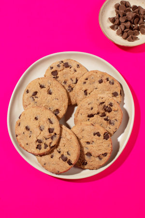 Chocolate chip cookie on a plate against a vivid pink background