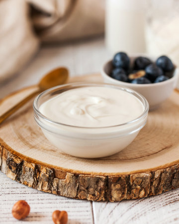 Rich creamy yogurt in a glass bowl on a wooden round, accompanied by fresh blueberriesの写真素材