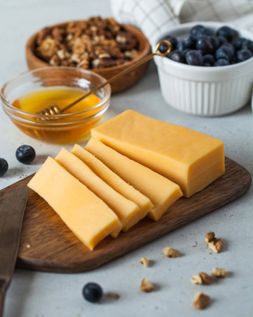 Sliced cheese on a wooden board with honey and blueberriesの写真素材