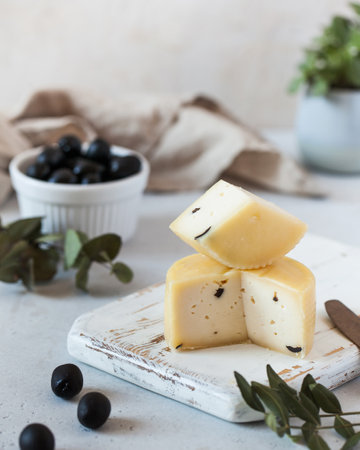 Stacked Caciotta cheese with black olives, presentation on a white distressed cutting boardの写真素材