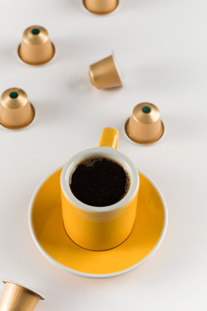 Yellow coffee cup with golden coffee capsules on a white background.の写真素材