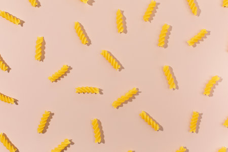 Flat lay of uncooked fusilli pasta arranged in a pattern on a pastel pink backgroundの写真素材
