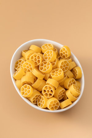 Uncooked rotelle pasta in a bowl on a beige background, Italian cuisine.