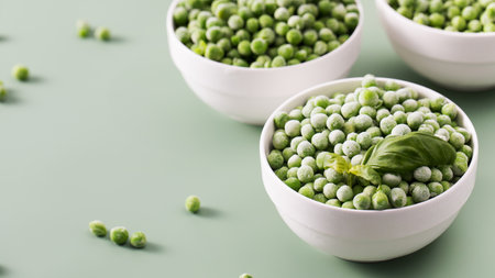 Three white bowls filled with frozen green peas on green background.の写真素材