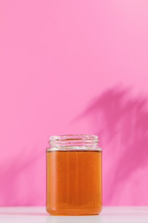 A jar of honey rests on a pink background, symbolizing the sweetness and purity of natureの写真素材