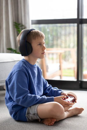 Young boy wearing headphones, focused on video game in living room. Video games