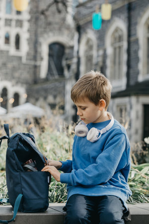 Smiling boy student with wireless earphones opens schoolbagの写真素材