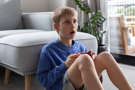 An astonished boy holds a game controller in hands, reacting to a video game. leisure, video gamesの写真素材