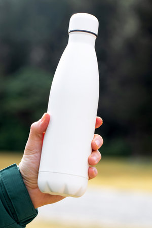 man holds mockup thermos against blurry bushes closeup