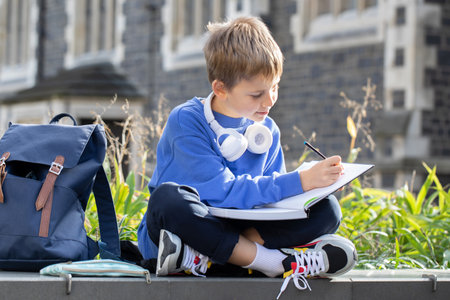 Diligent little boy with wireless earphones does homework