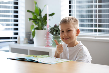 A cheerful boy happily gives a thumbs up while sitting at a table with a book.の写真素材