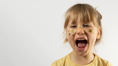 Cute young schoolgirl with golden stars on cheeks screams. Copy space