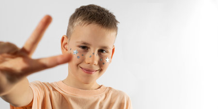 Happy teenager boy with stars on face shows peace gestures. Copy space