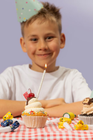 Smiling boy wearing birthday hat and decorated cupcake